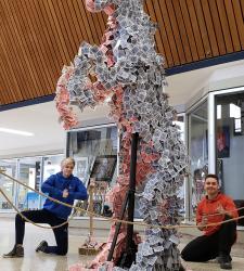 Two students beside their tall horse sculpture made of playing cards