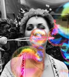 A black-and-white image of a person blowing coloured bubbles